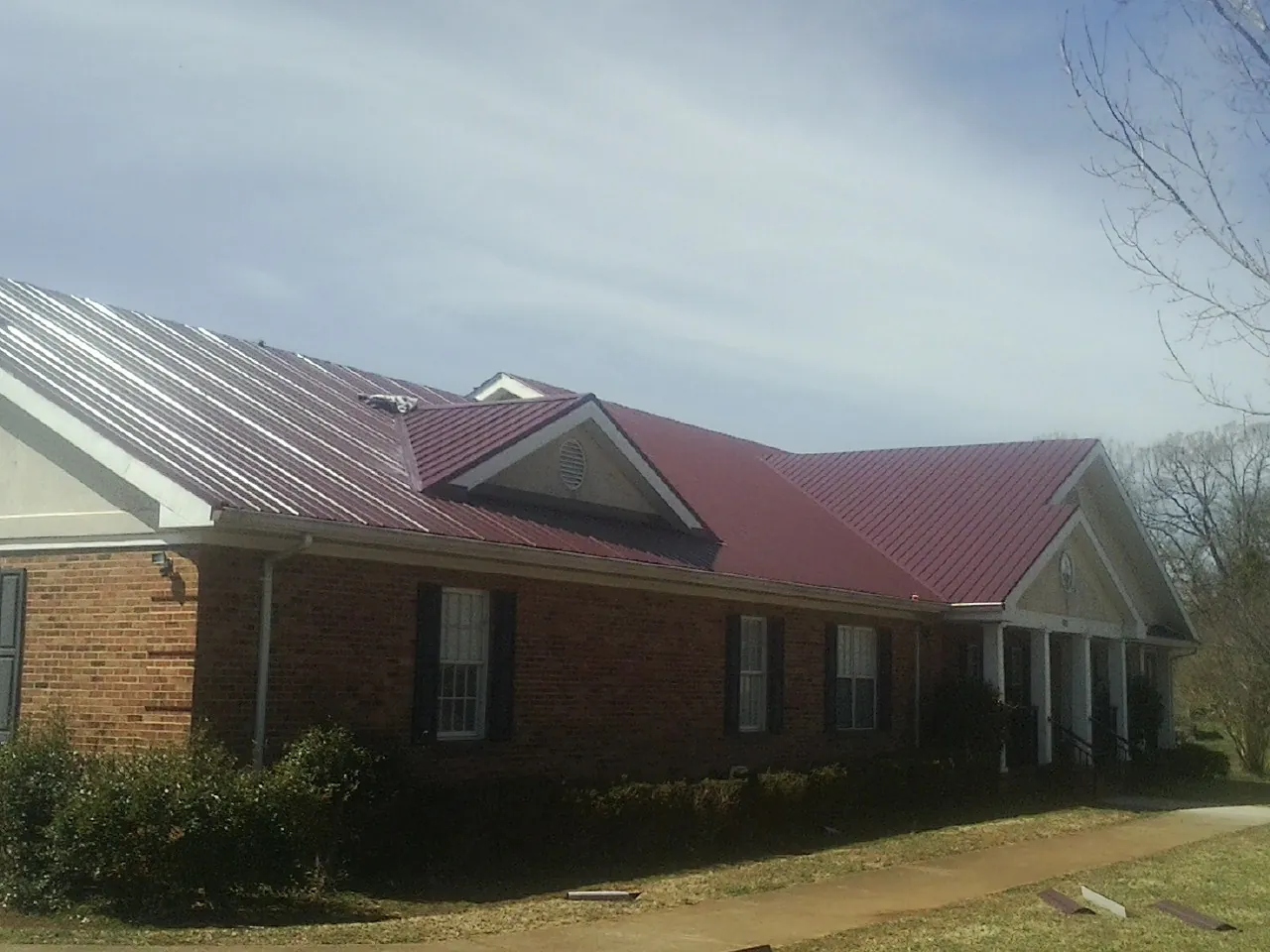 Red metal roof with gabled entries on a long brick building, from a Hail Damage Roof Repair job in Deerfield